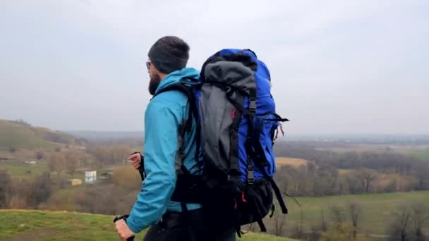 Hombre turista en chaqueta azul con mochila y bastones de trekking camina al aire libre — Vídeo de stock