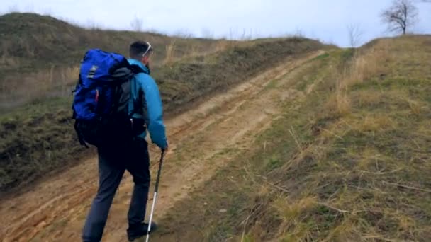 Турист в синей куртке с рюкзаком и палками прогуливается на свежем воздухе — стоковое видео