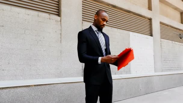 Hombre de negocios afroamericano de pie con la tableta al aire libre — Vídeos de Stock