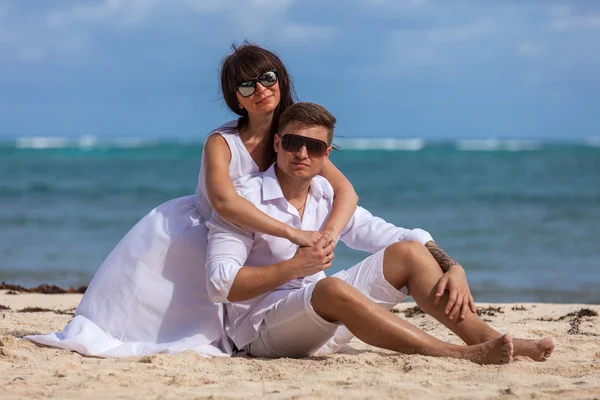 Young couple sitting together on a sand by ocean — Stock Photo, Image