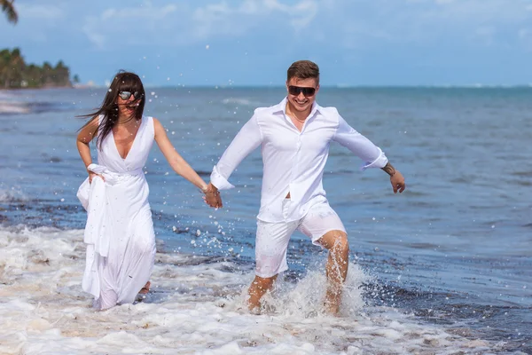 Casal correndo através de ondas em férias na praia — Fotografia de Stock