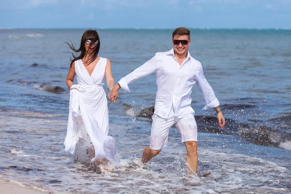 Pareja corriendo a través de olas en vacaciones en la playa —  Fotos de Stock