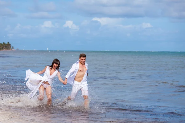 คู่รักวิ่งผ่านคลื่นในวันหยุดชายหาด — ภาพถ่ายสต็อก