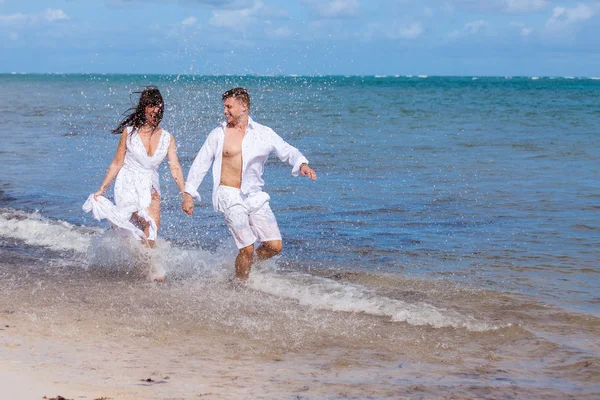 Casal correndo através de ondas em férias na praia — Fotografia de Stock
