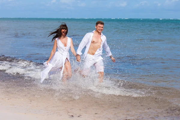 Casal correndo através de ondas em férias na praia — Fotografia de Stock