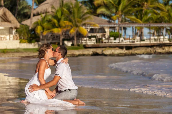 Young couple sitting together on a sand by ocean — Stock Photo, Image