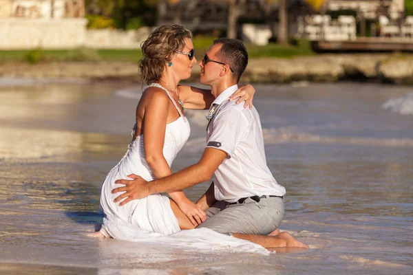 Young couple sitting together on a sand by ocean — Stock Photo, Image