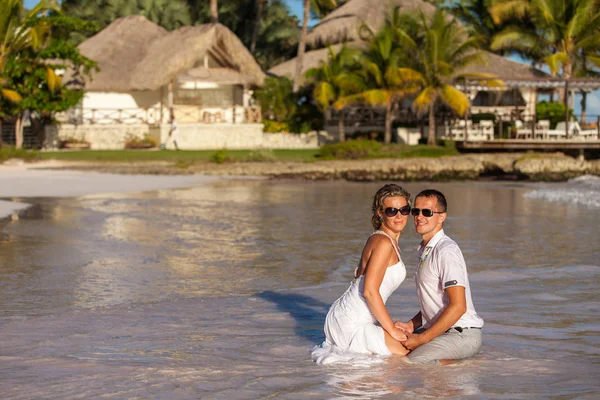 Young couple sitting together on a sand by ocean — Stock Photo, Image