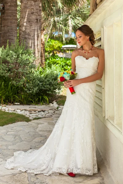 Sposa con fiori rimane vicino muro bianco — Foto Stock