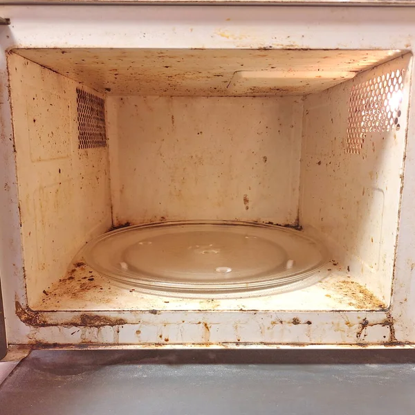 Terk edilmiş mutfak aletlerinin içinde kirli mikrodalga fırın lekeleri, yağ ve kir görünüyor..