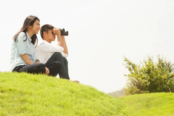 Asiatique jeune garçon et fille assis sur monticule recherche jumelles  . — Photo