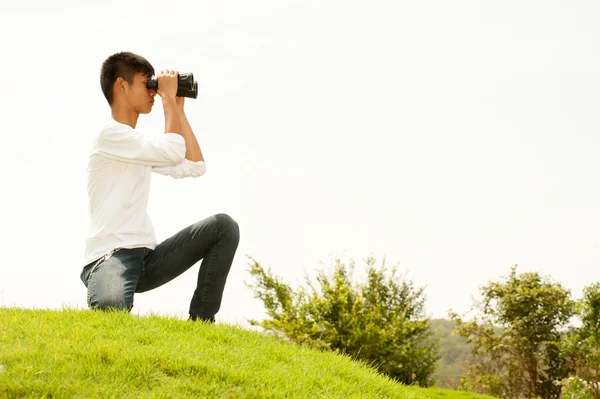 Asiatisk ung pojke sitta på högen söker kikare . — Stockfoto