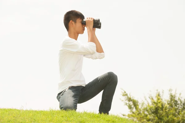 Asiatisk ung pojke sitta på högen söker kikare . — Stockfoto