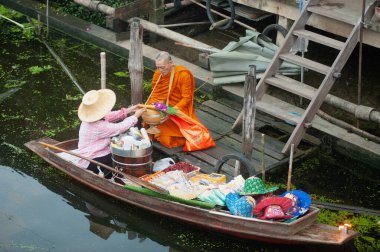 RATCHABURI, THAILAND-NOVEMBER 15, 2020: Kimliği belirsiz satıcılar Tayland ve yabancı turistler tarafından sevilen ünlü eski bir yüzen pazar olan Khlong Damnoen Saduak 'taki Budizm nedeniyle rahiplere sadaka verdiler.