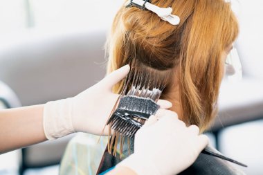 Bir kadın kuaförün, bir güzellik salonunda kızıl saçlıya kuaförlük yapması. Kuaförde saç şekillendirme işlemi. 