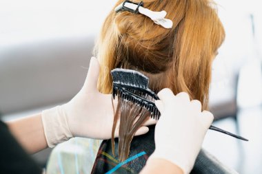 Bir kadın kuaförün, bir güzellik salonunda kızıl saçlıya kuaförlük yapması. Kuaförde saç şekillendirme işlemi. 