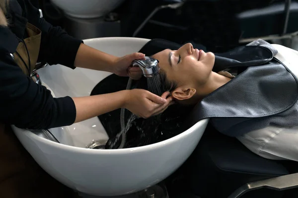 A hairdresser washes hair for a customer in a barber shop and women lying on a chair in a robe which takes care of the hair and scalp professionally.