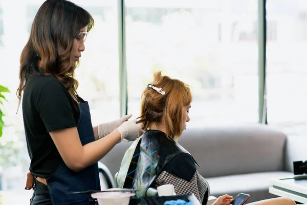 Hairdressers, working in salons with COVID-19 safety measures, are cutting and trimming the hair of a client who wears face shield a salon mask.