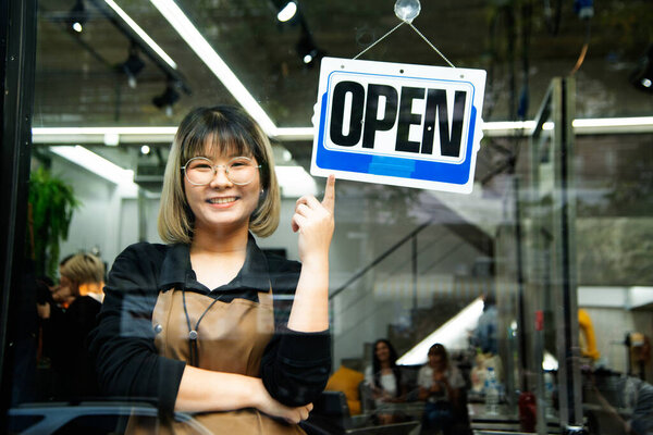 Asian female hairdesser of salon shop turning round open sign on a door.