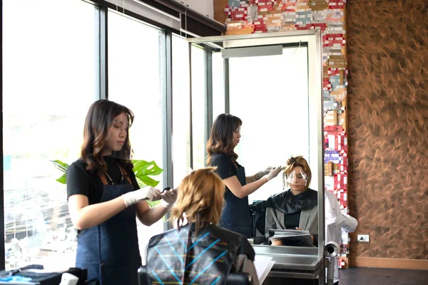 Asian female hairdresser make hairstyles for lady customers in modern beauty salons in Bangkok city.