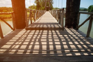Gündüz vakti, Tayland 'da bir parktaki su deposunu aşan ahşap asma köprüsünde karanlık bir gölge..