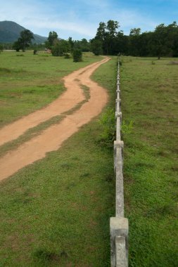 Dağ yolu ve beton çitler yeşil çimenler ve yumuşak bulutlarla çim tepeleri arasında süzülüyor..