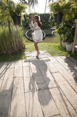 Genç ve güzel Asyalı kadın parkta salıncakta sallanıyor..