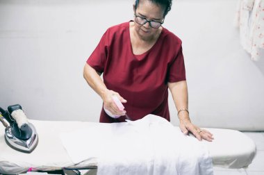 An elderly woman who is a housewife folding clothes at the laundry.