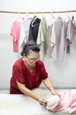 An elderly woman who is a housewife folding clothes at the laundry.