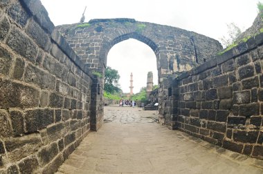 AURANGABUD, INDIA - 25 AUG 2025: Daulatabad kalesindeki Chand Minar 'da (Ay Kulesi) kimliği belirsiz bir turist, ortaçağ askeri mimarisi ve kültür mirası sergilenen devasa taş duvarlarla inşa edildi..