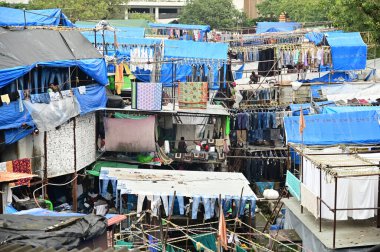 MUMBAI, INDIA - 26 AĞUSTOS 2025: Dhobi Ghat 'te çamaşır ipine kıyafet asan kimliği belirsiz bir işçi dünyaca ünlü ve simgesel bir açık hava çamaşır alanıdır..