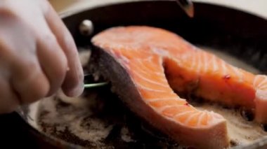 Şefin elleri balık bifteğini enfes bir şekilde çeviriyor. Biberiyeyle birlikte tereyağında kızartılmış. Balık gastronomisi. Tavada biftek kızartma
