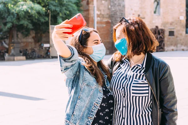 Yüz maskeli bir çift kadın şehirde selfie çekerken eğleniyor.