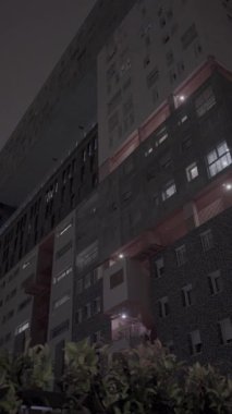 Geceleri çağdaş bir apartman kompleksinin solucan bakışı. Ön cephe pek çok pencereyi gösteriyor. Işıklar açık, kentsel yaşam hissi yaratıyor.