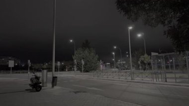 Geceleyin ıssız bir caddede tek bir araba geçiyordu. Modern sokak lambaları boş yolu ve park etmiş bir scooter 'ı aydınlatıyor