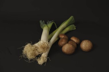 Ham pırasa ve kahverengi krema mantarları, sağlıklı doğal besin bileşenlerini temsil eden koyu bir arka planda dizilmiştir.