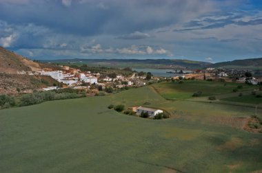 Arcos de La Frontera 'nın beyaz köyünü, yeşil tarlaları ve bulutlu gökyüzünün altındaki rezervuarı ele geçirmek, geleneksel mimari ve doğayı gözler önüne seriyor.