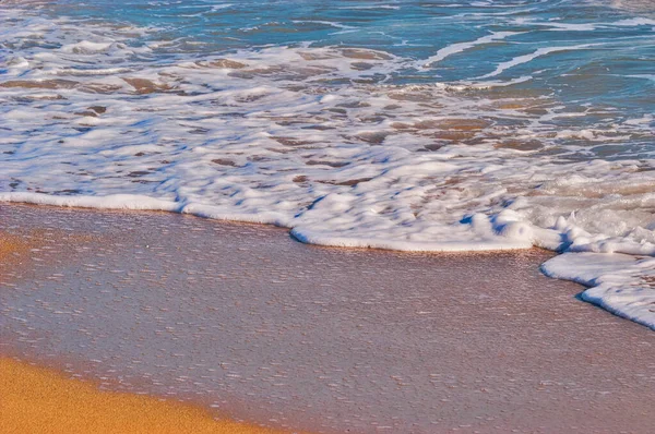 Okyanus dalgaları kumlu bir plajın kıyılarında beyaz köpük oluşturuyor. Doğal su hareketi rahatlatıcı ve sakinleştirici.