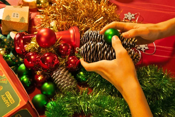 Noel süsleri, çam kozalakları ve altın rengi süslemeleri bayram dekorasyonu ve hazırlıkları için masa üstüne dizen eller.