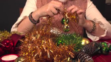 Şenlikli bir çelenk hazırlayan kadın elleri. Tatil sezonu için altın süslemelere parlak yeşil ve altın takılar takıyor.