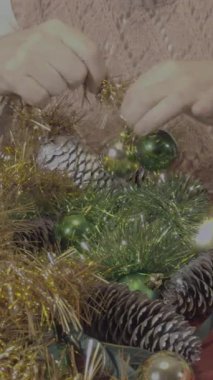 Bir insanın ellerini kapatın ve geleneksel bir Noel çelengi hazırlayın. Çam kozalakları, altın süslemeler, yeşil ve altın takılar.