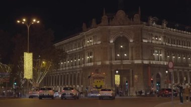 İspanya, Madrid, 127, 2025, İspanya 'nın Madrid kentindeki aydınlatılmış İspanya Bankası' nın önünden geçen araçlar ve yayalar.