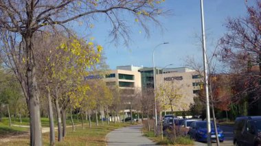 İspanya, Madrid, 12 / 01 / 2025: Güneşli bir günde modern bir bina ve 5G baz istasyonunun yanında araba kullanan şehir sokak manzarası