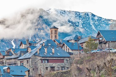 Geleneksel tahta çatılı tarihi Boi Taull köy evleri ve bulutlu Pireneler dağlarının altına kurulmuş bir Roma çan kulesi.