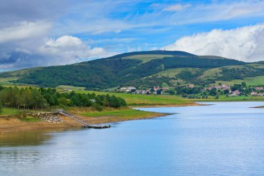 Ebro rezervuarı alçak su seviyesi, kıyıda bir rıhtım ve yeşil tepelerin arasına kurulmuş bir köy ile genişliyor.