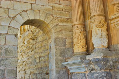 Antik Romence detaylar, dokulu taş duvarlar, yuvarlak bir kemer ve oyulmuş kabartmalar ve desenlerle dekoratif sütunlar sergiliyor.