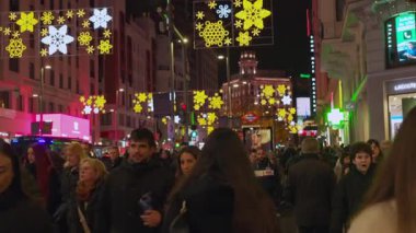 Madrid, İspanya, Noel, 12-14-2025: Yılbaşı kar taneleri aydınlatmalarıyla süslenmiş isimsiz bir kalabalık gece bir şehir caddesinde yürüyor