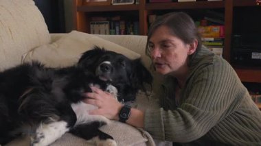 Bir kadın kanepede siyah beyaz bir köpeği okşuyor. Köpek uzanıyor ve rahatlıyor.