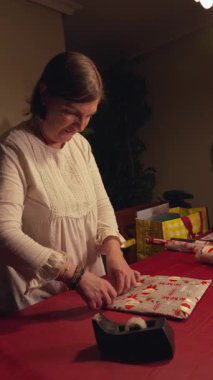 Bir kadın hediye paketini bant kutusuyla paketliyor. Gülümsüyor ve bu süreçte eğleniyor gibi görünüyor.