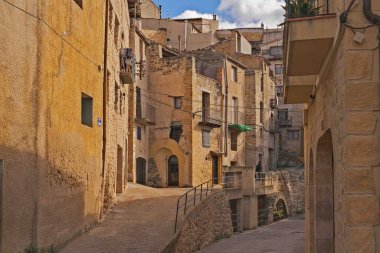 Bir tarafında taş bir duvar, diğer tarafında taş bir bina olan dar bir sokak. Sokak binalarla dolu ve taş bir geçidi var.